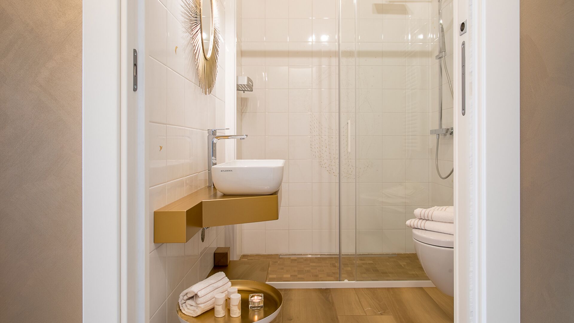 A modern bathroom with a white sink, a gold vanity, a glass shower enclosure, and a toilet.