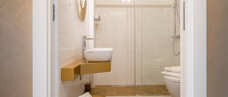 A modern bathroom with a white sink, a gold vanity, a glass shower enclosure, and a toilet.