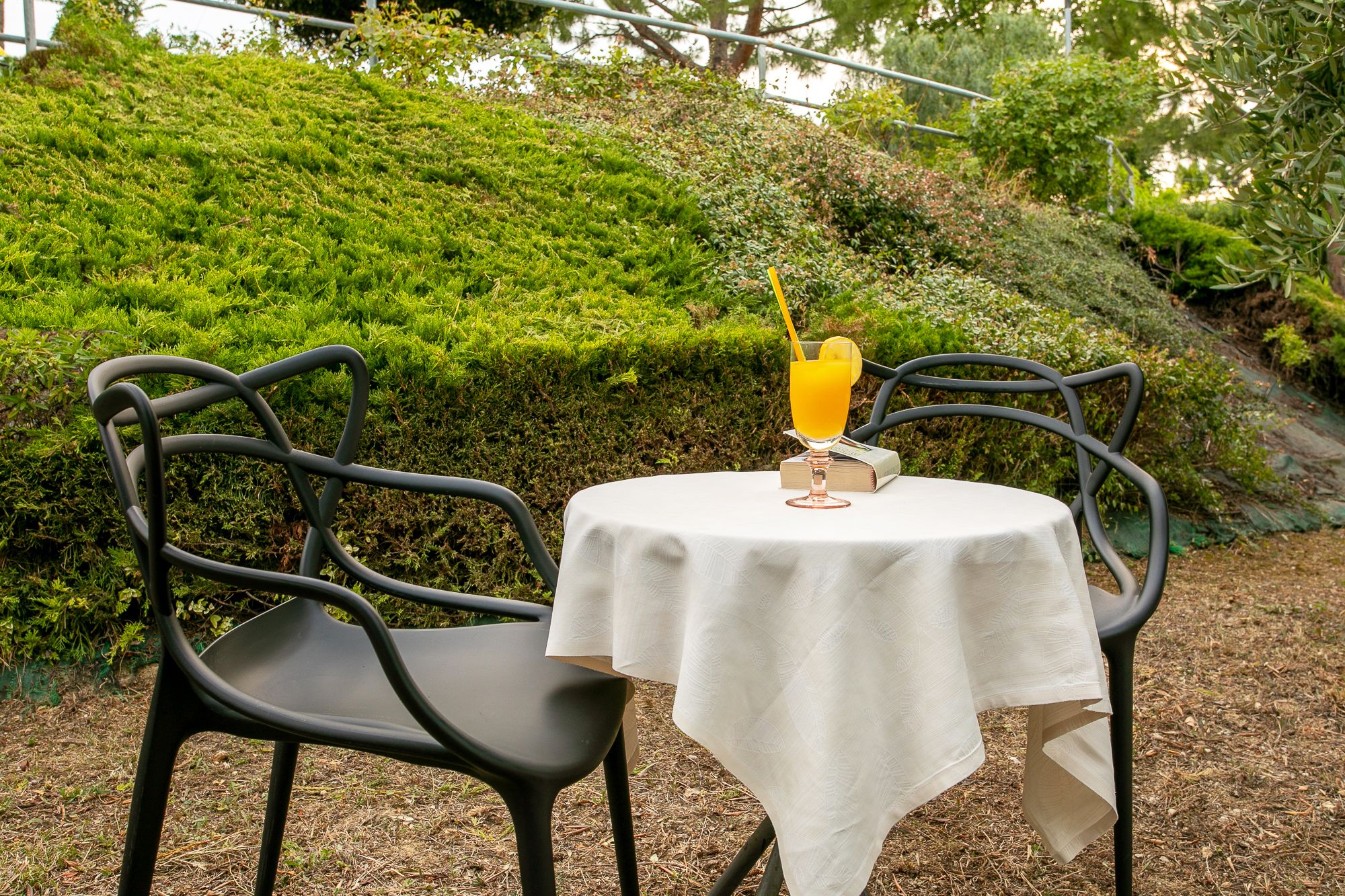 Ein Tisch mit weißer Tischdecke, zwei schwarze Metallstühle und ein Glas Orangensaft mit Trinkhalm.