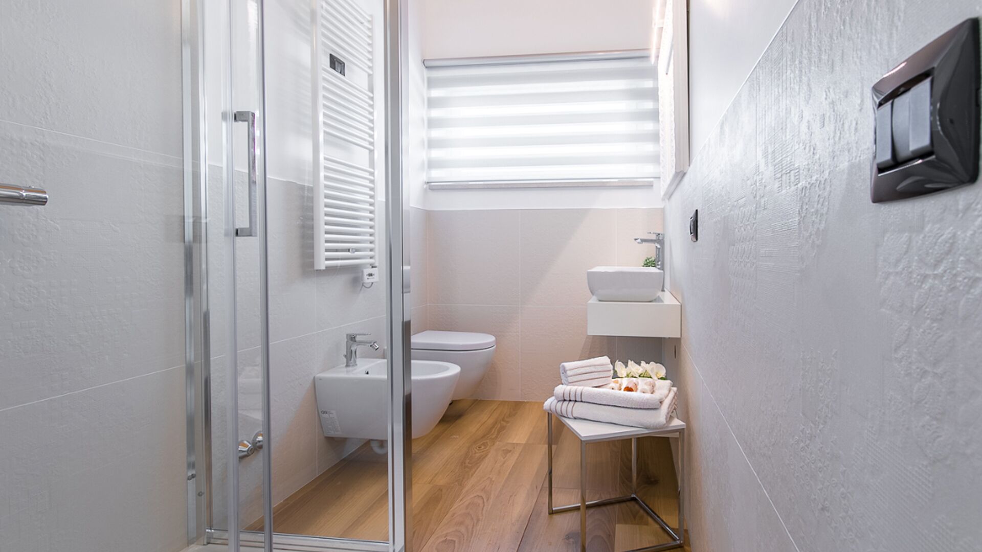 A modern bathroom with a glass shower door, a toilet, a sink, and a towel rack with folded towels.