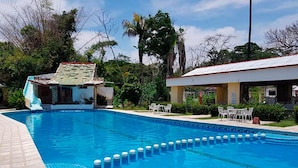 A swimming pool with a clear blue water feature, a small waterfall, and a covered seating area with chairs. - Villas Kin Ha (Palenque)