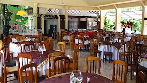 A restaurant with multiple tables and chairs, a stage, and a logo on the wall. - Villas Kin Ha (Palenque)
