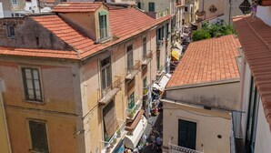 A narrow street with buildings on either side, balconies, and a small market area with people and goods. - Caruso Suite (Sorrento)
