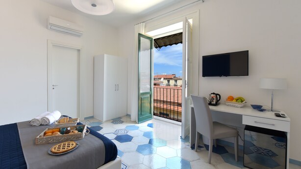 A hotel room with a bed, a desk, a TV, and a balcony with a view. - Caruso Suite (Sorrento)