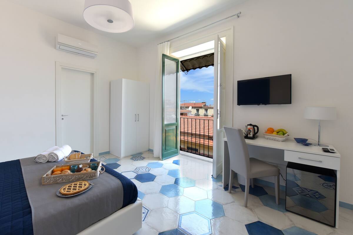 A hotel room with a bed, a desk, a TV, and a balcony with a view.