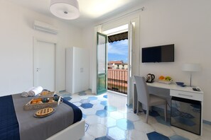 Una habitación de hotel con cama, escritorio, televisión y balcón con vistas.