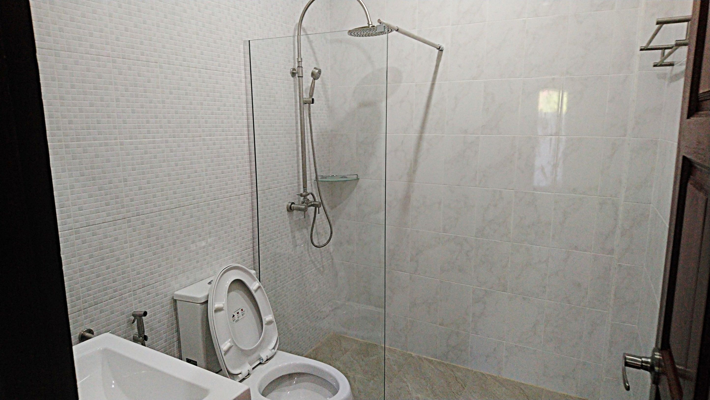A bathroom with a toilet, a shower with a glass door, and a tiled wall.