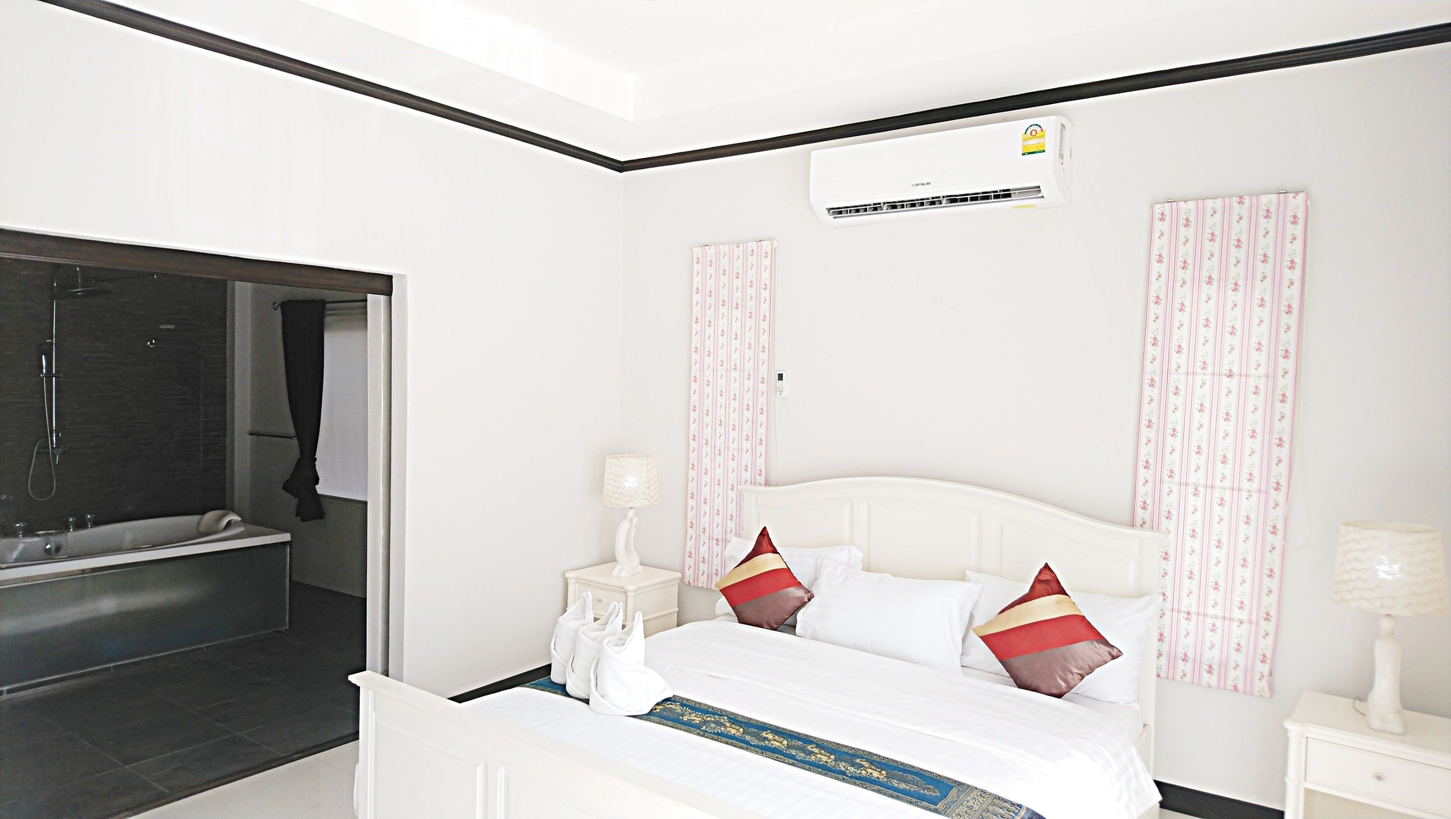 A hotel room with a bed, a nightstand, a lamp, a shower area, and a wall-mounted air conditioner.