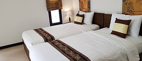 A hotel room with two beds, a window with curtains, a nightstand with a lamp, and a headboard with a floral pattern.