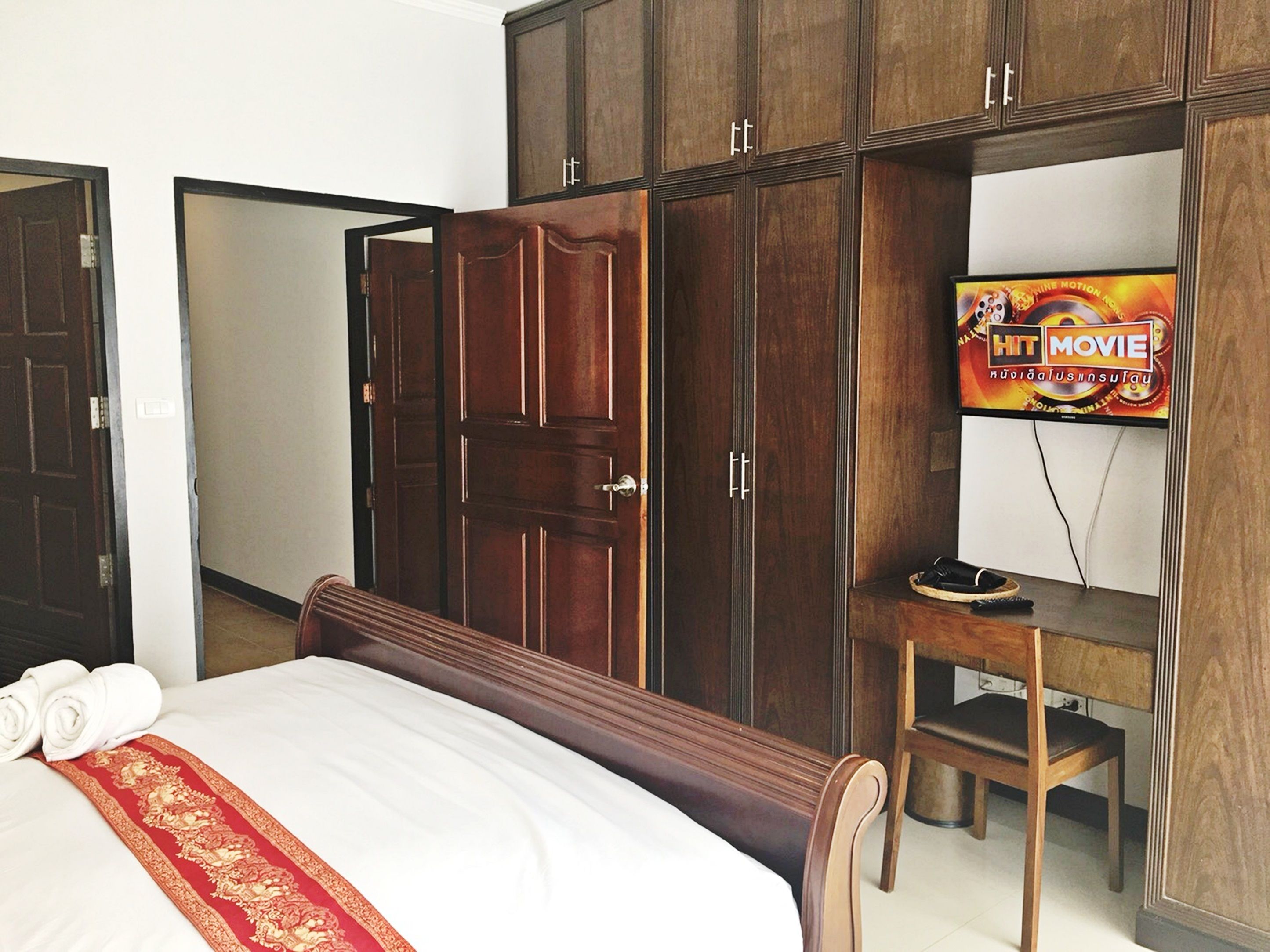 Hotellihuone, jossa on sänky, puinen vaatekaappi, televisio ja pieni työpöytä.