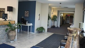 A modern hotel lobby with a stone wall, a reception desk, a coffee machine, and several potted plants. - R & R Inn & Suites (Camrose)