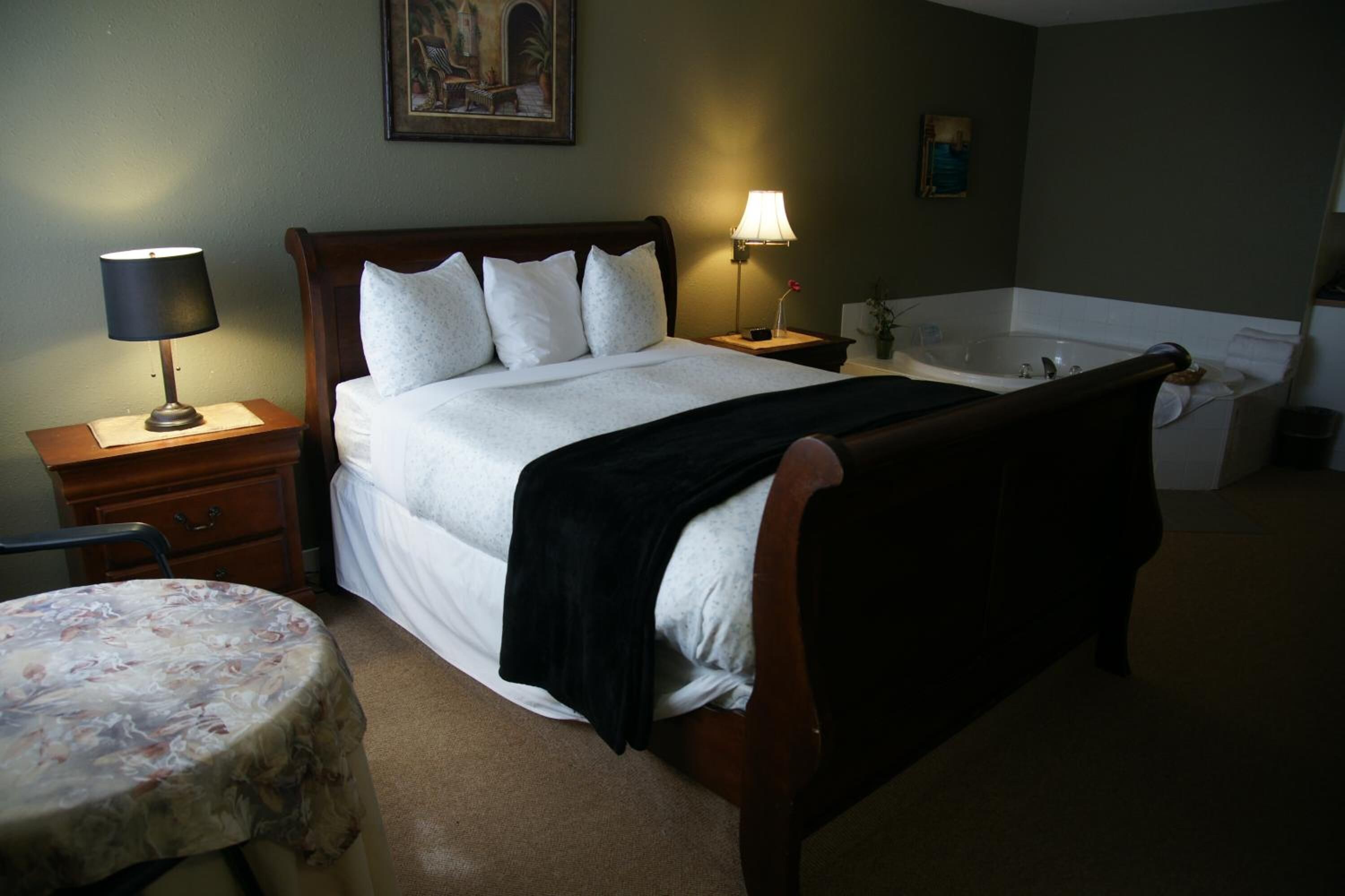 A hotel room with a bed, bedside tables, a round table, and a bathtub.