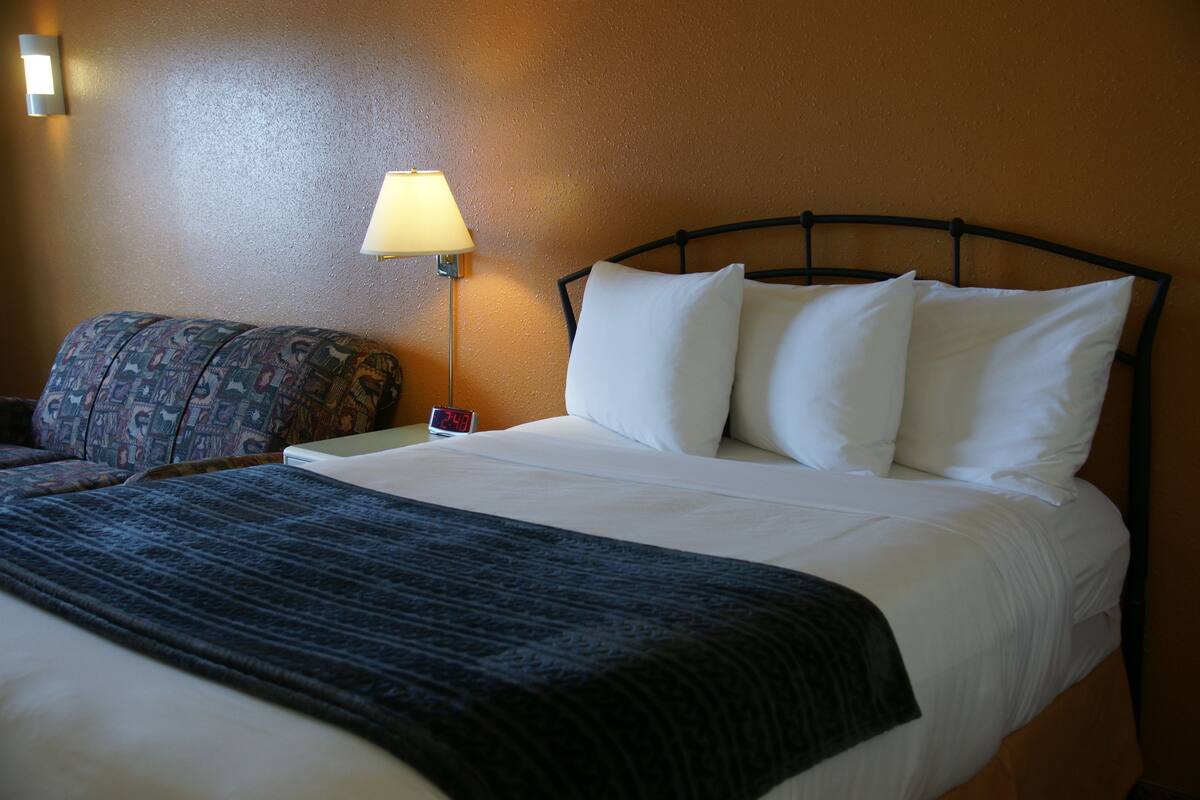 Quarto de hotel com uma cama, mesa de cabeceira, abajur e relógio.