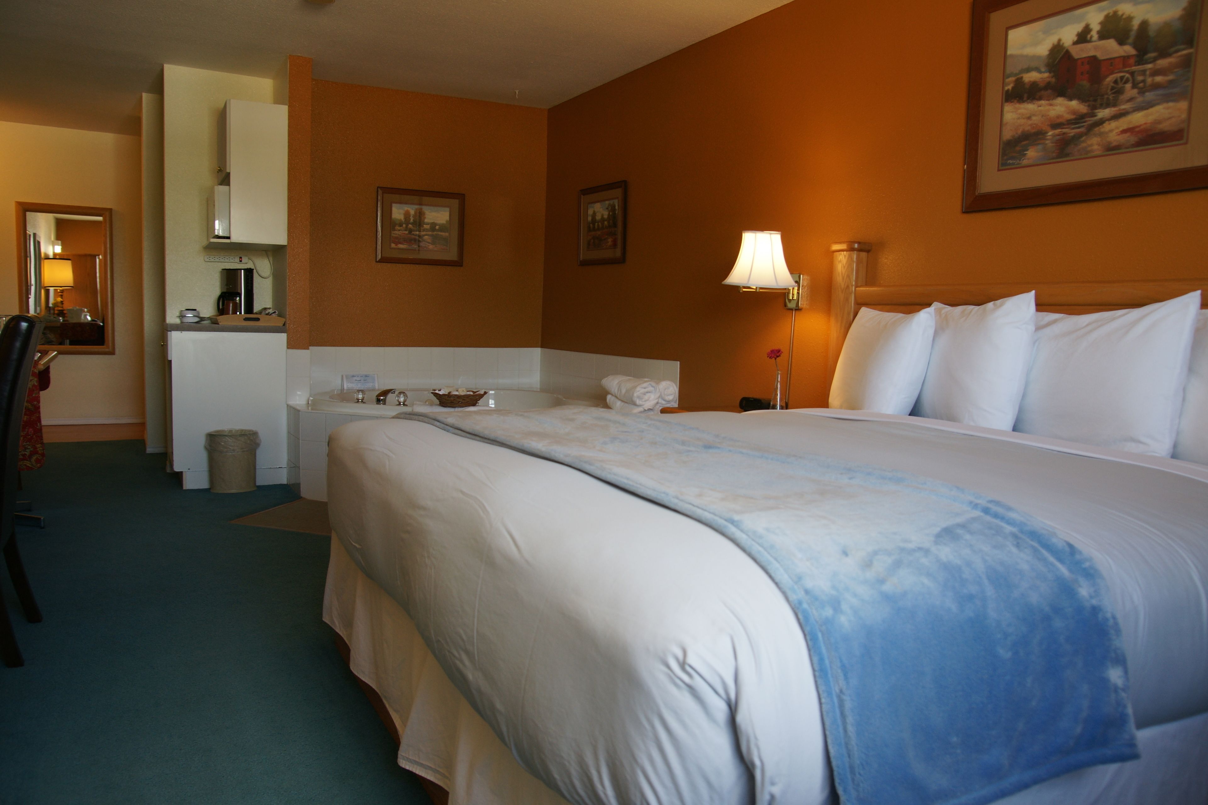 A hotel room with a large bed, a desk with a chair, a small kitchenette, and a bathroom.