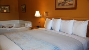 A hotel room with a large bed, a bathtub, and a nightstand with a lamp. - R & R Inn & Suites (Camrose)