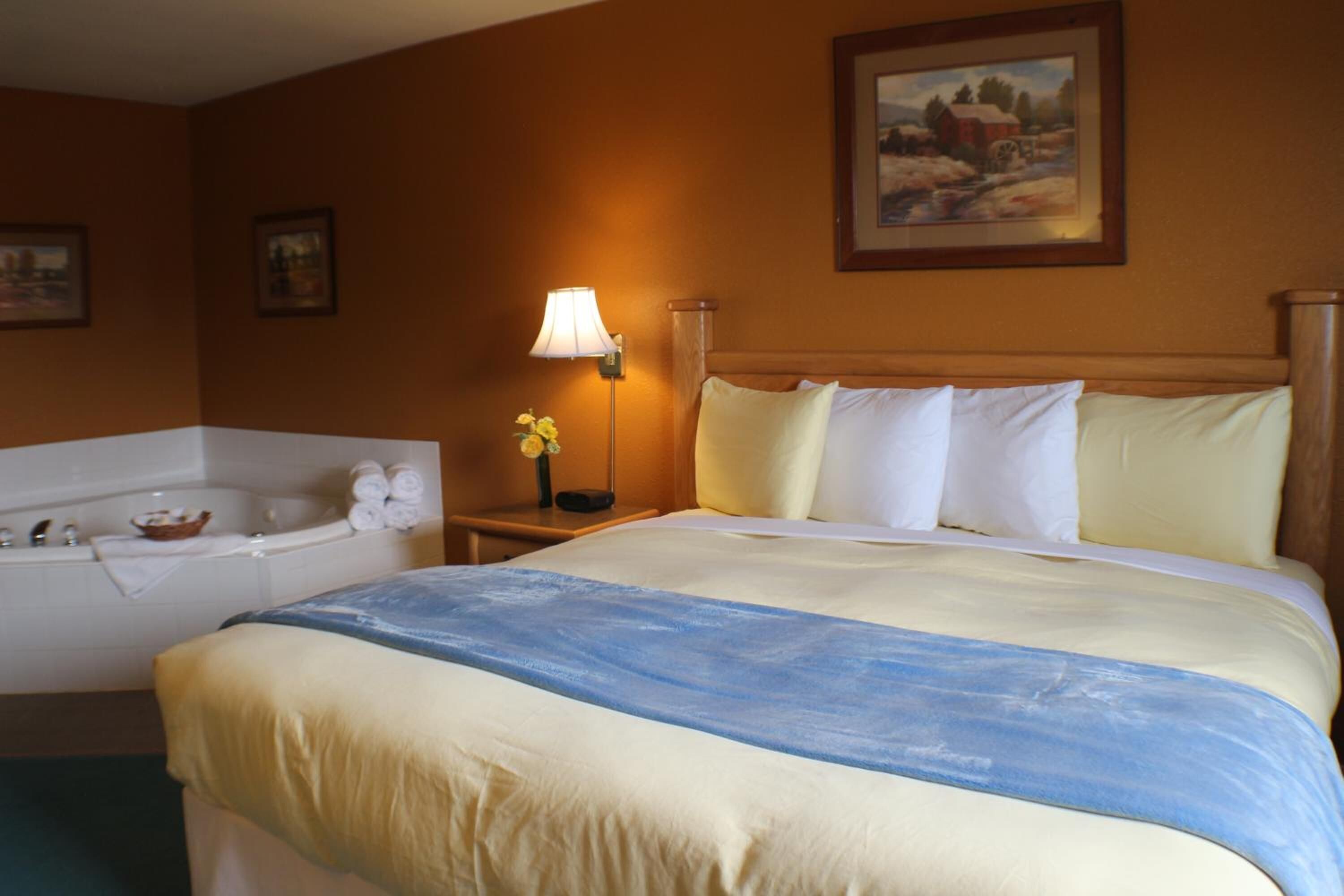 A hotel room with a large bed, a separate bathroom with a bathtub, and a painting on the wall.