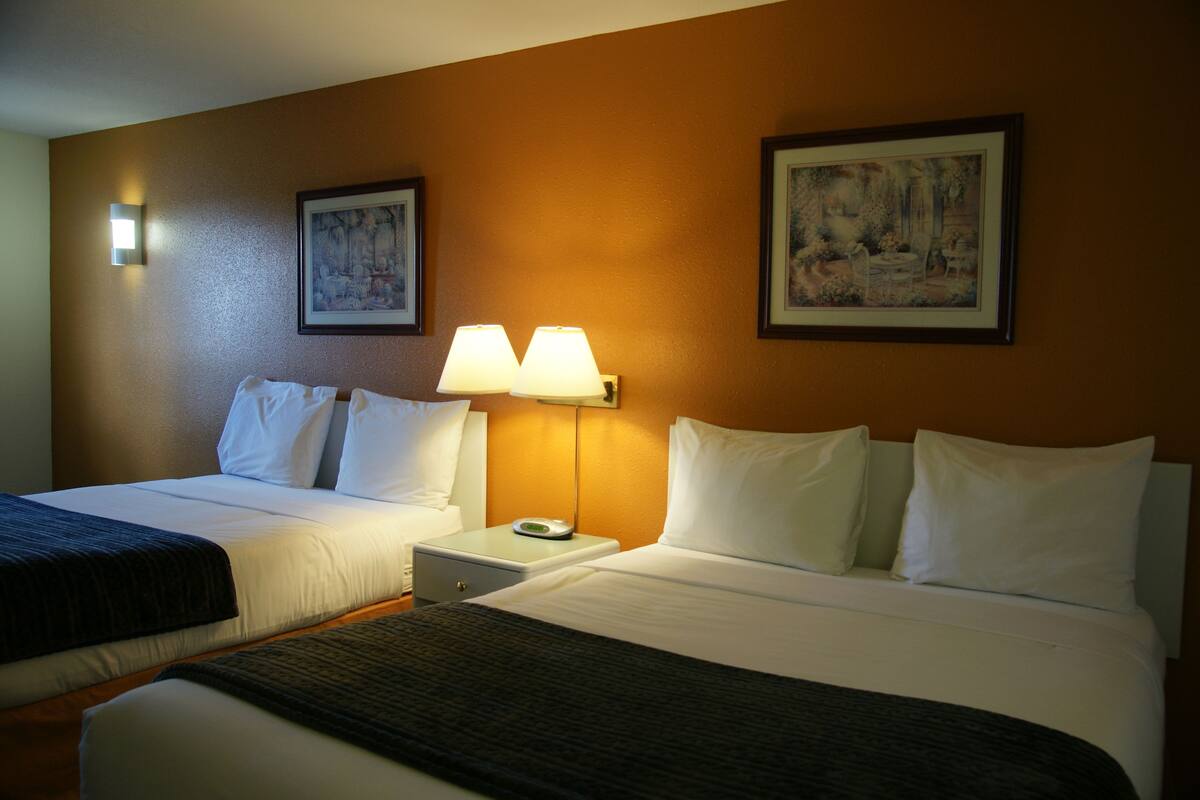 Quarto de hotel com duas camas, uma mesa de cabeceira, um abajur e duas imagens emolduradas na parede.