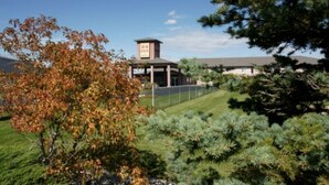 A hotel with a tower-like structure, surrounded by a well-maintained lawn and various trees. - R & R Inn & Suites (Camrose)