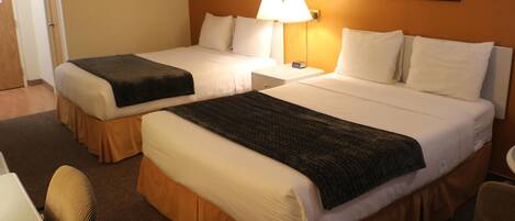 Une chambre d’hôtel avec deux lits, un bureau, une chaise et une lampe.