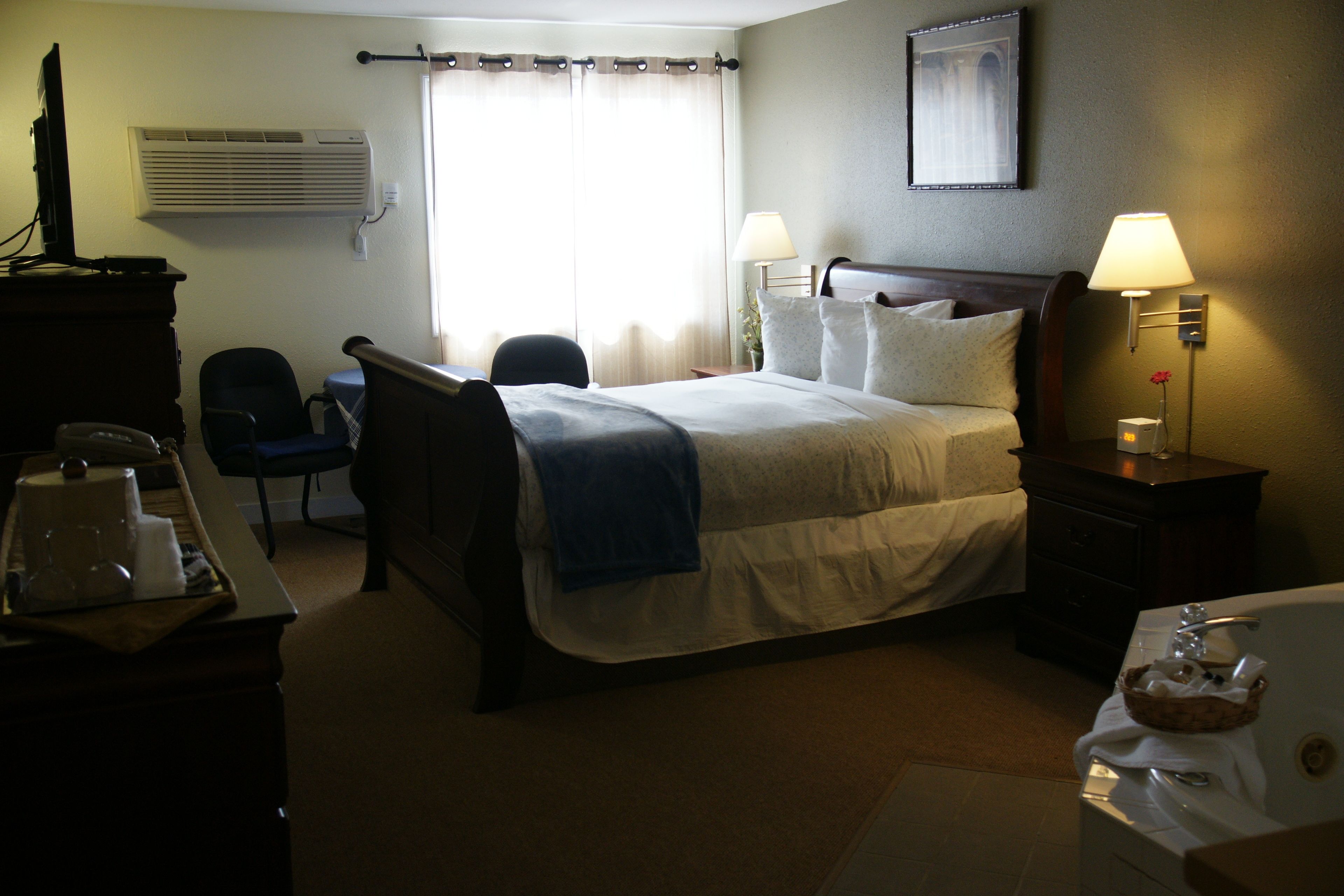 A hotel room with a bed, bedside lamps, a desk with a computer, a chair, and a bathroom with a bathtub.
