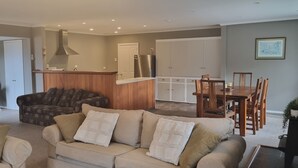 A living room with a beige sofa, a patterned sofa, and a dining area with a wooden table and chairs.