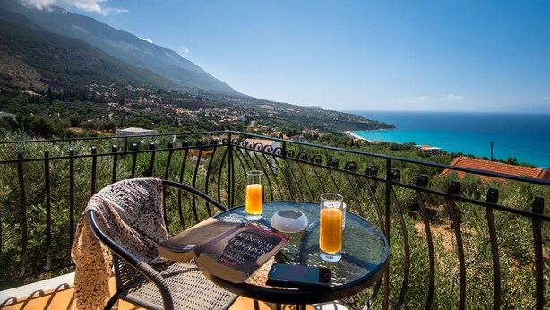 A balcony with a table, two glasses of orange juice, a book, and a smartphone. - Lourdas amazing view - Studio Marinos. (Vlachata)