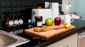 A kitchen counter with a cutting board, a knife, a jar of jam, a green apple, a red apple, a banana, and a white mug. - Lourdas amazing view - Studio Marinos. (Vlachata)