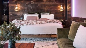 A modern bedroom with a wooden headboard, a large bed with multiple pillows, a green armchair, and two hanging light fixtures. - Ranked in the World's Top 60 Places to Elope (Hepburn Springs)