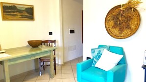 Een kamer met een houten eettafel, een blauwe fauteuil met een wit kussen en een geweven wanddecoratie.