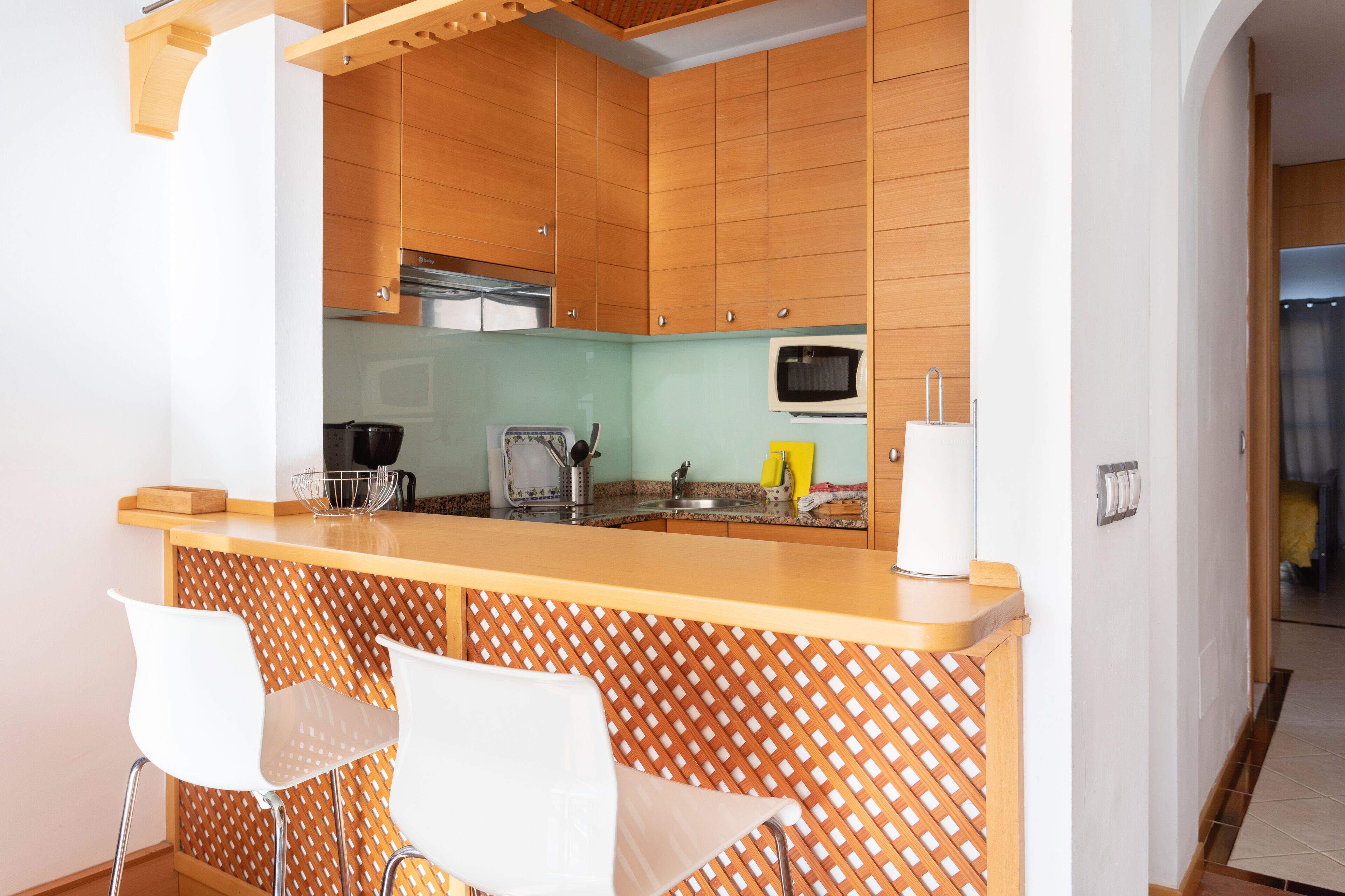 A modern kitchen with wooden cabinets, a central island with bar stools, and a microwave.