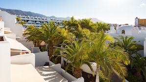 Un resort con edificios blancos, palmeras y montañas al fondo.