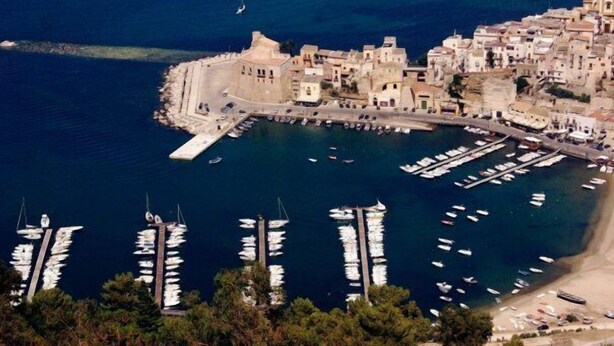 Une ville côtière dotée d’un port de plaisance rempli de bateaux, de bâtiments historiques et d’une imposante forteresse.