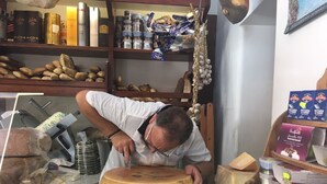 Une salle d’affinage du fromage, avec une meule de fromage, des étagères remplies de produits emballés et une tête d’ail suspendue.