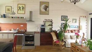 Eine kleine Küche mit Herd, Backofen und Spüle. Es gibt einen Essbereich mit einem Stuhl und Tisch. Der Raum hat Holzböden und eine hohe Decke mit freiliegenden Balken.