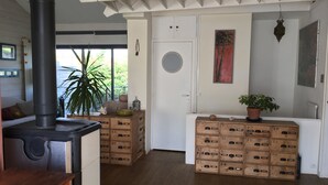 Ein gemütliches Zimmer mit Kaminofen, Holzregalen, einer Topfpflanze und Blick ins Grüne.