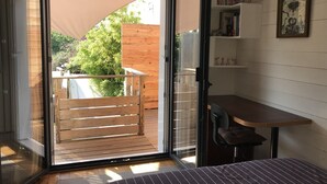 Ein Zimmer mit einer Glasschiebetür, die auf eine Holzdiele führt, einem Bett mit gestreifter Bettwäsche, einem kleinen Tisch und einem Bücherregal mit Büchern und Dekoration.