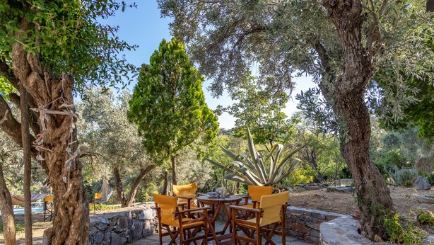 An outdoor patio with stone flooring, wooden chairs, and a table. - Country Villa Kalimera | Private Hilltop Villa in Skopelos with Pool & Views (skopelos)