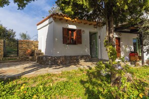 Una casa rústica con pared de piedra, puerta de madera y ventana con contraventanas de madera.