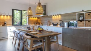 A modern kitchen with a wooden dining table, white chairs, and pendant lighting. - House / Villa - SAINT-TROPEZ (La Croix-Valmer)