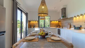 A modern kitchen with a dining table set for six, a large window, and a hanging light fixture. - House / Villa - SAINT-TROPEZ (La Croix-Valmer)