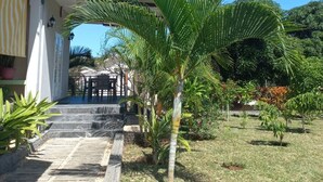 Um edifício com entrada coberta, um caminho de pedra que leva a uma área de estar e um pequeno jardim com palmeiras.