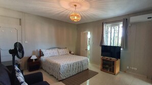 Quarto com cama, um suporte para televisão, um ventilador e uma janela com cortinas.