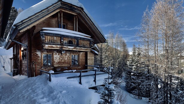 Une cabane en bois, dotée d’un toit en pente, entourée d’arbres couverts de neige et sous un ciel dégagé.