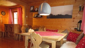 L’intérieur d’un chalet en bois chaleureux et accueillant, avec une table à manger, des chaises, un canapé et un luminaire suspendu.