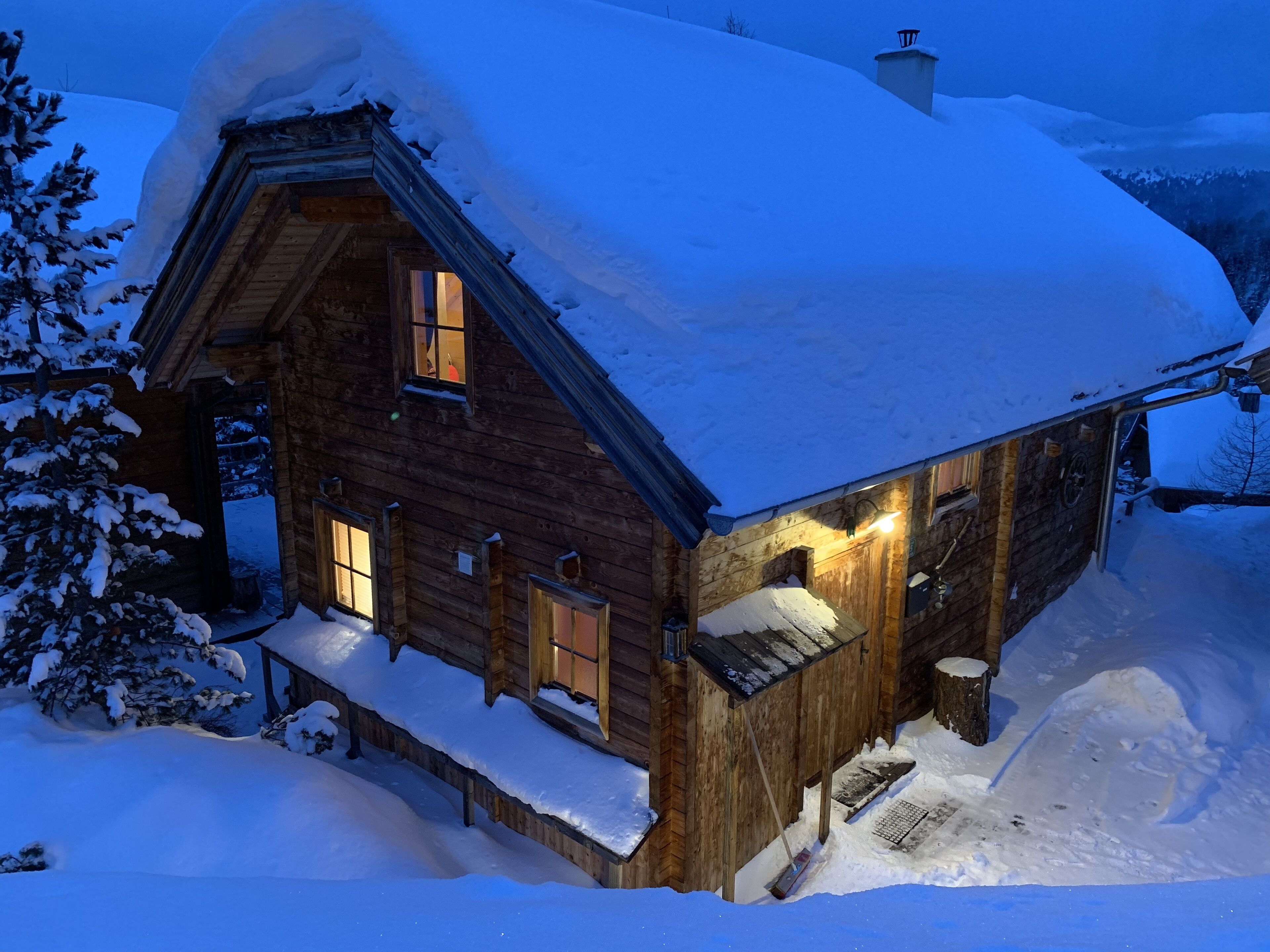 Een houten hutje met een met sneeuw bedekte dak en een verlicht interieur, omgeven door sneeuw.