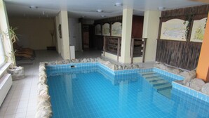Une piscine intérieure à l’eau d’un bleu limpide, avec des marches en pierre et un sol carrelé.