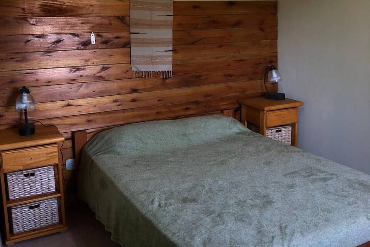 Una cama individual con cabecera de madera, dos mesitas de noche con lámparas y una estantería en la pared.