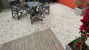 A covered patio with a wooden table and chairs, a barbecue grill, and a red brick wall.