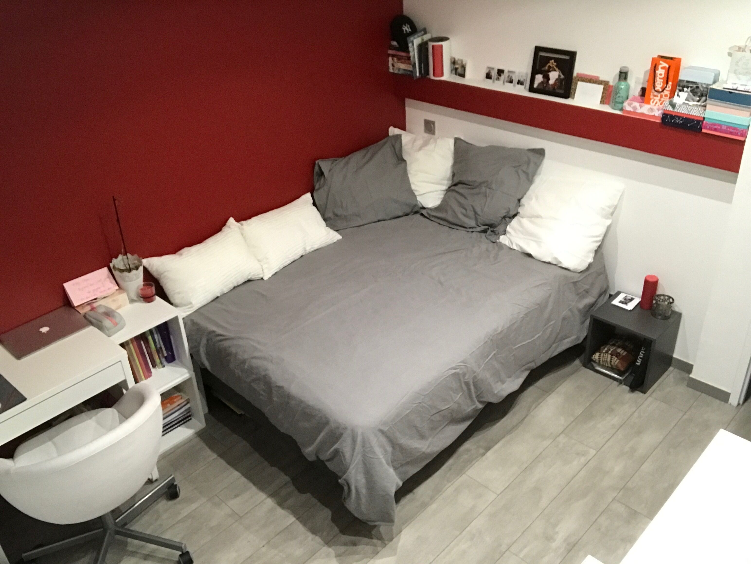 Une chambre bien rangée, avec un lit, un bureau et une chaise. On peut y voir des livres et des objets personnels sur les étagères.