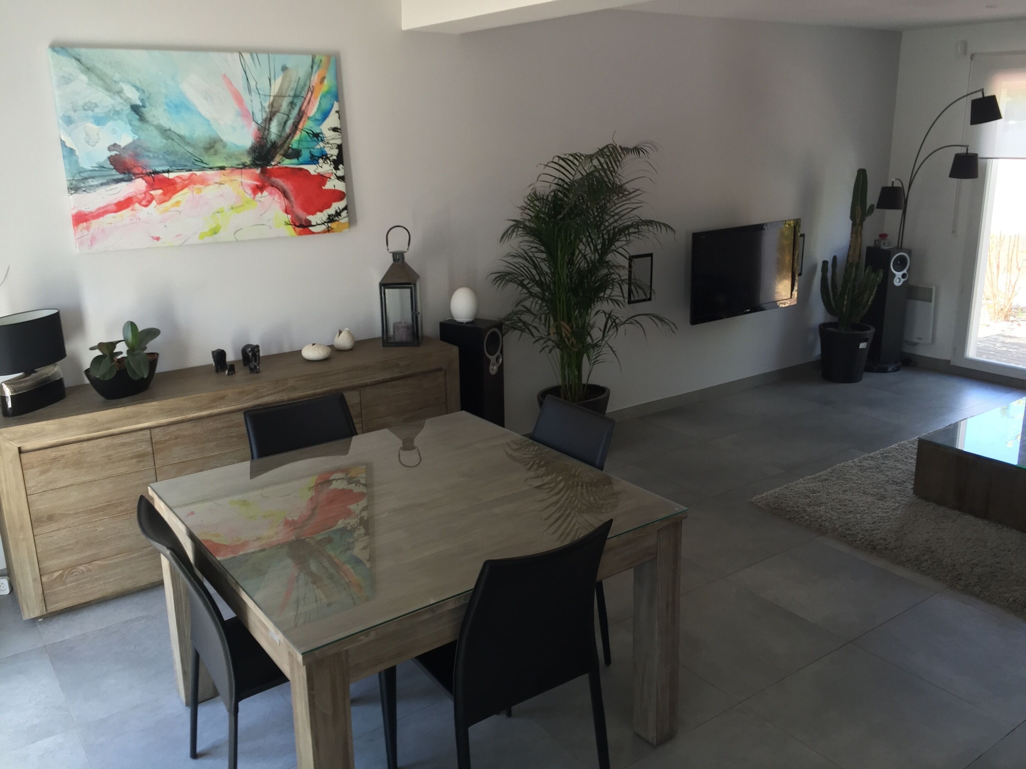 Un salon moderne comprenant une table à manger, des chaises, une grande peinture abstraite, une plante en pot, un téléviseur et un lampadaire.